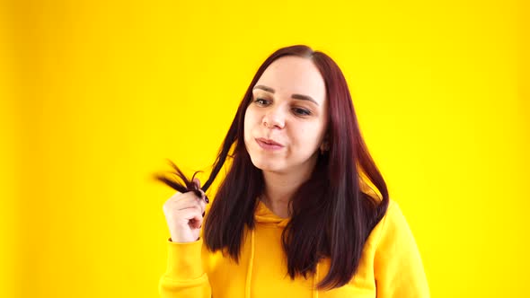 Close Up of Young Woman Twists Her Hair on Yellow Background