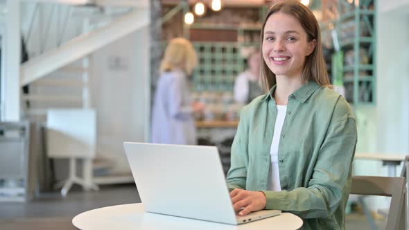 Woman with Laptop Smiling at Camera in Cafe 