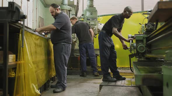 Caucasian and African American male factory worker standing at a workbench and operating machinery