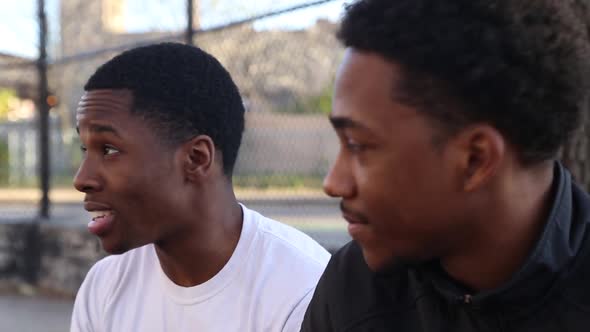 Two young basketball players talking on the sidelines of a street court.