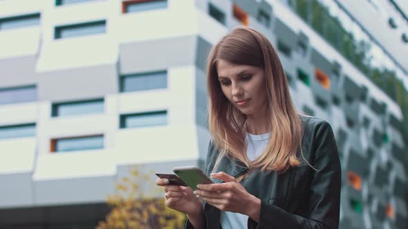 Smiling Young Female Customer Holding Credit Card and Smartphone on Modern Home