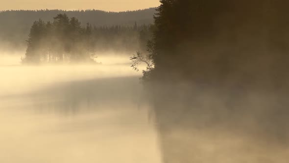 Foggy Morning at Finnish Lake. Smoke Moving Along Water Surface in Morning Sun Lights. Lapland