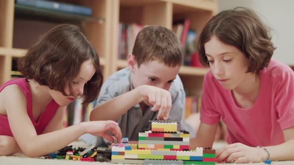 Three kids playing with toy plastic bricks at home