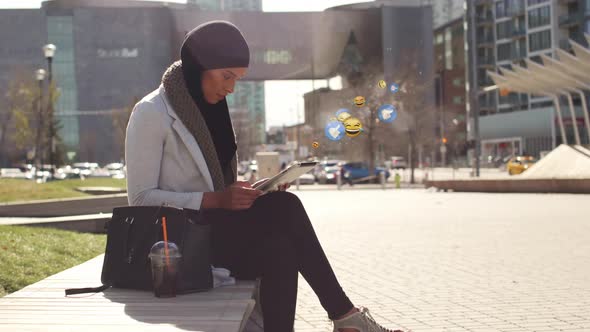 Animation of mixed race woman wearing hijab in street using tablet computer with floating emoji