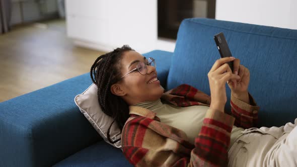 Happy African American Girl Relaxing on Sofa at Home with Smartphone