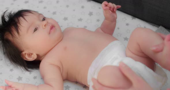 Mom Plays with a Newborn Baby in a Diaper Lying on His Back on a Baby Diaper