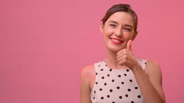 Young Caucasian Woman Raising Thumb Up on a Pink Background.