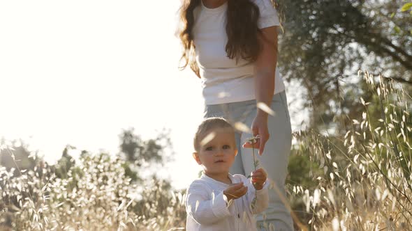 Little Blond Boy Holds Wild Flower Standing Near Mother