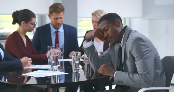 Tired Businessman Sleeping on Office Desk While His Colleagues Discussing in Meeting