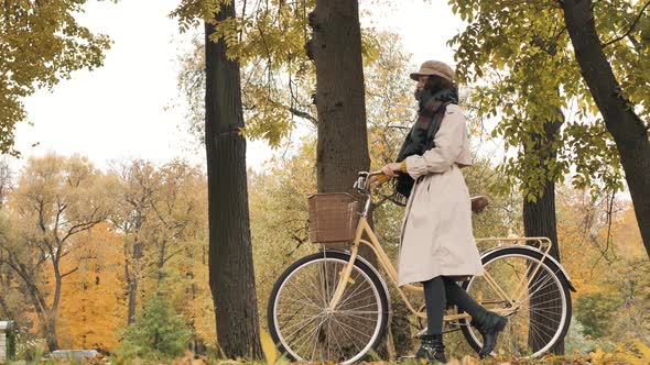 Young Woman Walks with Bike Against Yellow Trees in Park