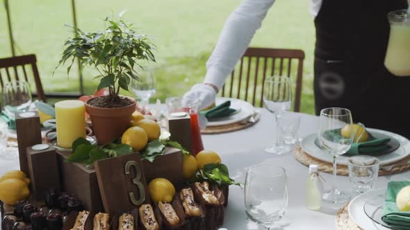 the Waiter on a Garden Catering Puts Juice and Lemonade on the Festive Table Decorated with Lemons