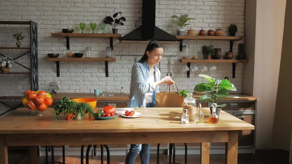 A Beautiful Young Woman in a Good Mood is Sorting Vegetables From a Bag and Putting Them on the