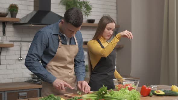 Happy couple enjoying cooking time together at home. Side view of young man cutting vegetables