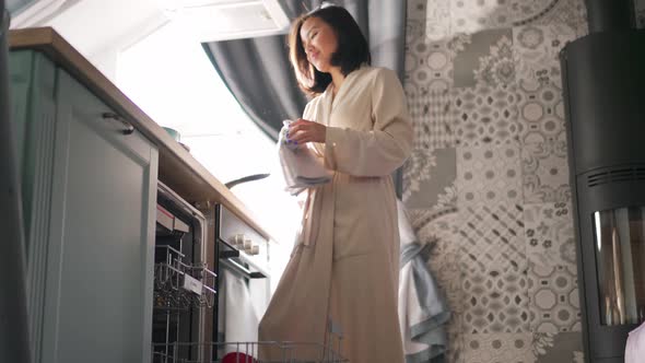 Asian woman wipes a cup with a dry cloth after washing in a dishwasher