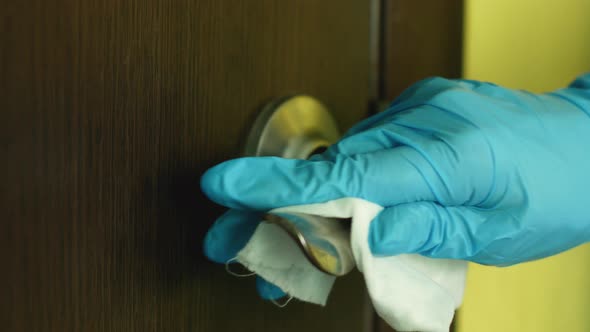 A hand in a medical glove wipes a door metal handle with a rag in a medical office.