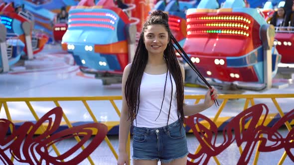 Attractive Girl with Pigtails of Hair on the Background of the Carousel