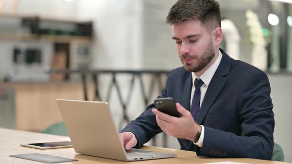 Young Businessman Using Smartphone and Laptop in Office