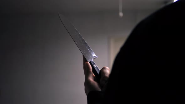 A scary slasher killer holding a terrifying knife in silhouette to attack his murder victim.