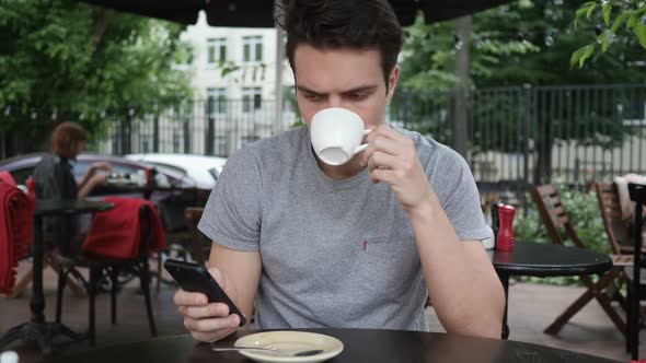 Man Drinking Coffee and Using Smartphone While Sitting in Cafe Terrace