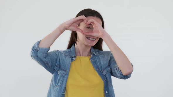 Cheerful Woman Smiling with Dental Brackets Folded Hands in Heart Form Looking Through White