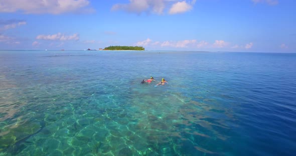 Aerial drone view of a man and woman couple snorkeling over the coral reef of a tropical island
