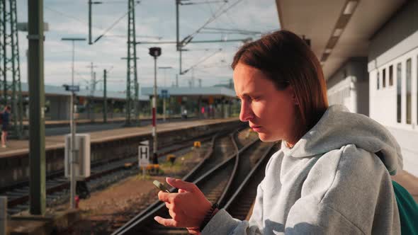 Portrait of woman standing on empty platform at railway station with smartphone in hands