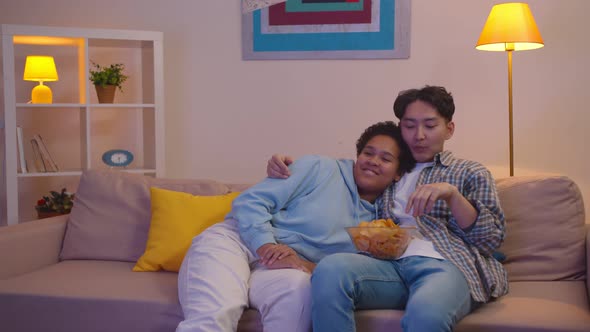 Charming Young Diverse Couple Sitting on the Couch and Watching Tv with Bowl of Chips