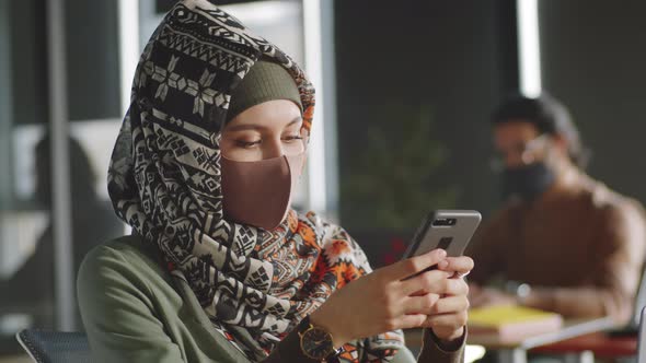 Businesswoman in Hijab and Mask Using Smartphone in Office