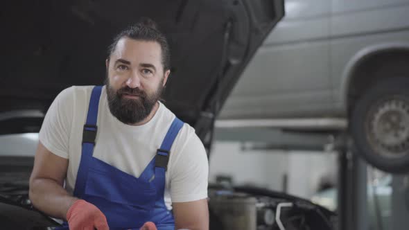 Portrait Attractive Bearded Mechanic Posing with Spanner Sitting on the Hood of a Broken Car