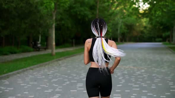 Rear View of European Woman with Black and White Dreadlocks Running By Local Green Park in the City