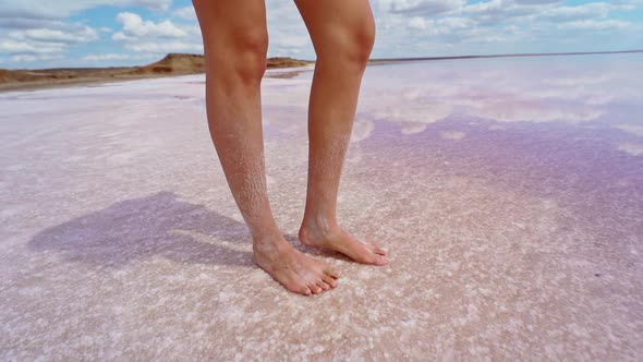 Female Long Legs with Salt on Skin Standing in Salt Pink Lake Reflection in Water of Cloudy Sky