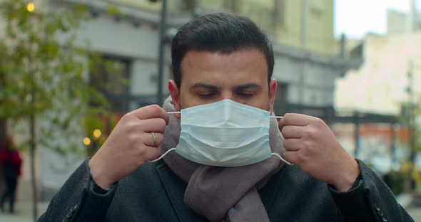 Young Man Out and About in the City Streets During the Day, Putting on a Face Mask Against Air