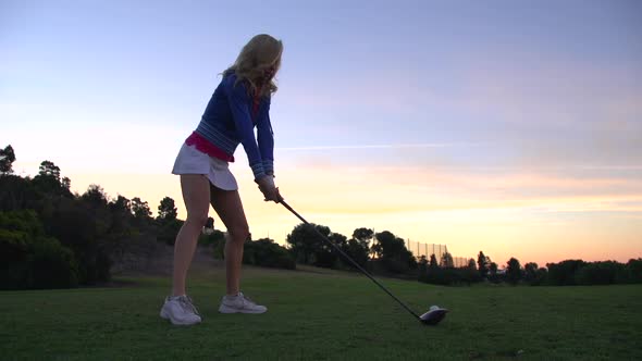 A woman teeing off while playing golf at sunset