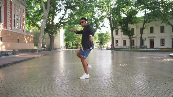 Young Stylish Hipster Black Man in White Headphones and Sun Glasses Dancing Outdoor in City Centre