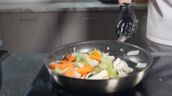Chef in Black Gloves Cooking Vegetables on Frying Pan in Restaurant Kitchen