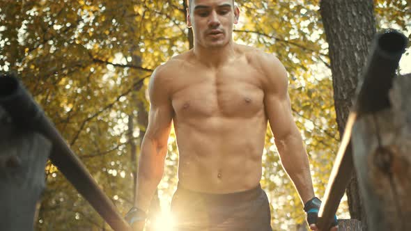 Muscular man doing push ups exercises on parallel bars. workout in the forest gym, outdoors.