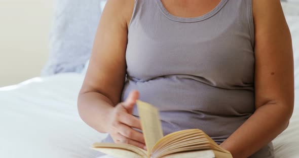 Happy senior woman reading book while sitting on bed in the bed room 4k