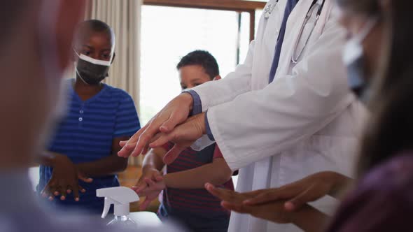 Diverse schoolteacher and schoolchildren standing disinfecting hands, all wearing face masks