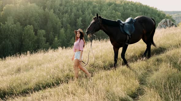 Beautiful Woman with Horse. Girl in Cowboy Hat Walks Next To the Horse, Stroking and Hugging Horse