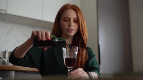 Closeup of Attractive Young Woman Pouring Alcohol Beverage in Glass in Kitchen with Modern Light