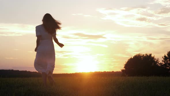 Free Happy Caucasian Woman In White Dress Runs Across Field To Meet The Sunset