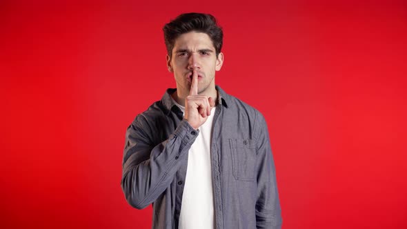 European Handsome Man Holding Finger on His Lips Over Red Background