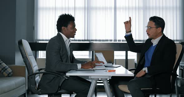 Two Young Businessman Talking at Desk in Office