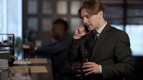 Busy Caucasian Businessman Entering Bar with Beer Bottle Talking on Phone As African American Client