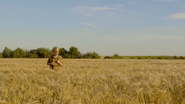 Caucasian Conceptual Man Farmer Agronomist in a Hat Goes and Looking to a Wheat Field