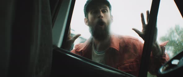 Man with hat knocks on car window waving and laughing