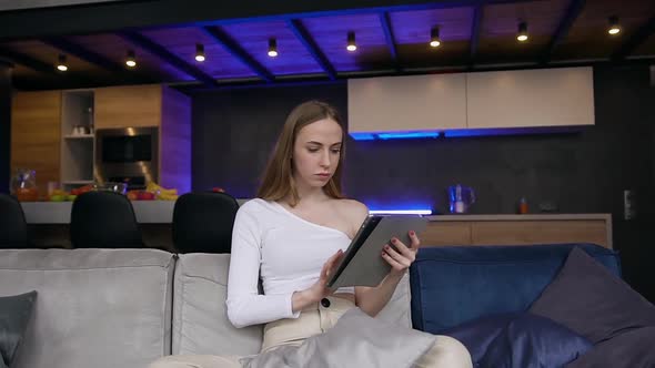 Woman in Stylish Clothes Sitting on the Sofa at Home and Browsing Apps on i-pad