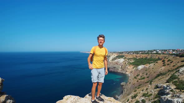 Young Man Traveler in Orange T-shirt Standing on Cliff Edge