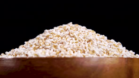 Puffed amaranth seeds in wooden bowl. Popped amaranthus grain on a black background. Macro