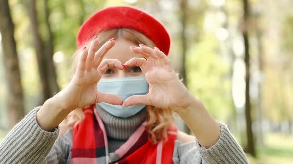 Pretty Woman in Disposable Mask Showing Heart Sign in Autumn Park